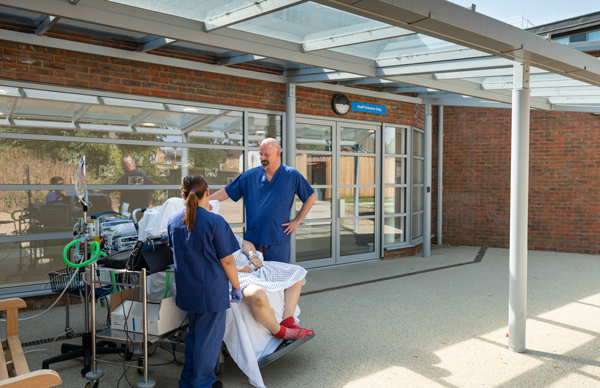 Mr Andre Simon speaking with a patient and staff member outside in new sun lounge area 