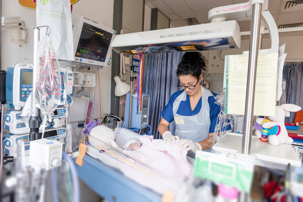 Paediatric nurse in PICU with baby in an incubator